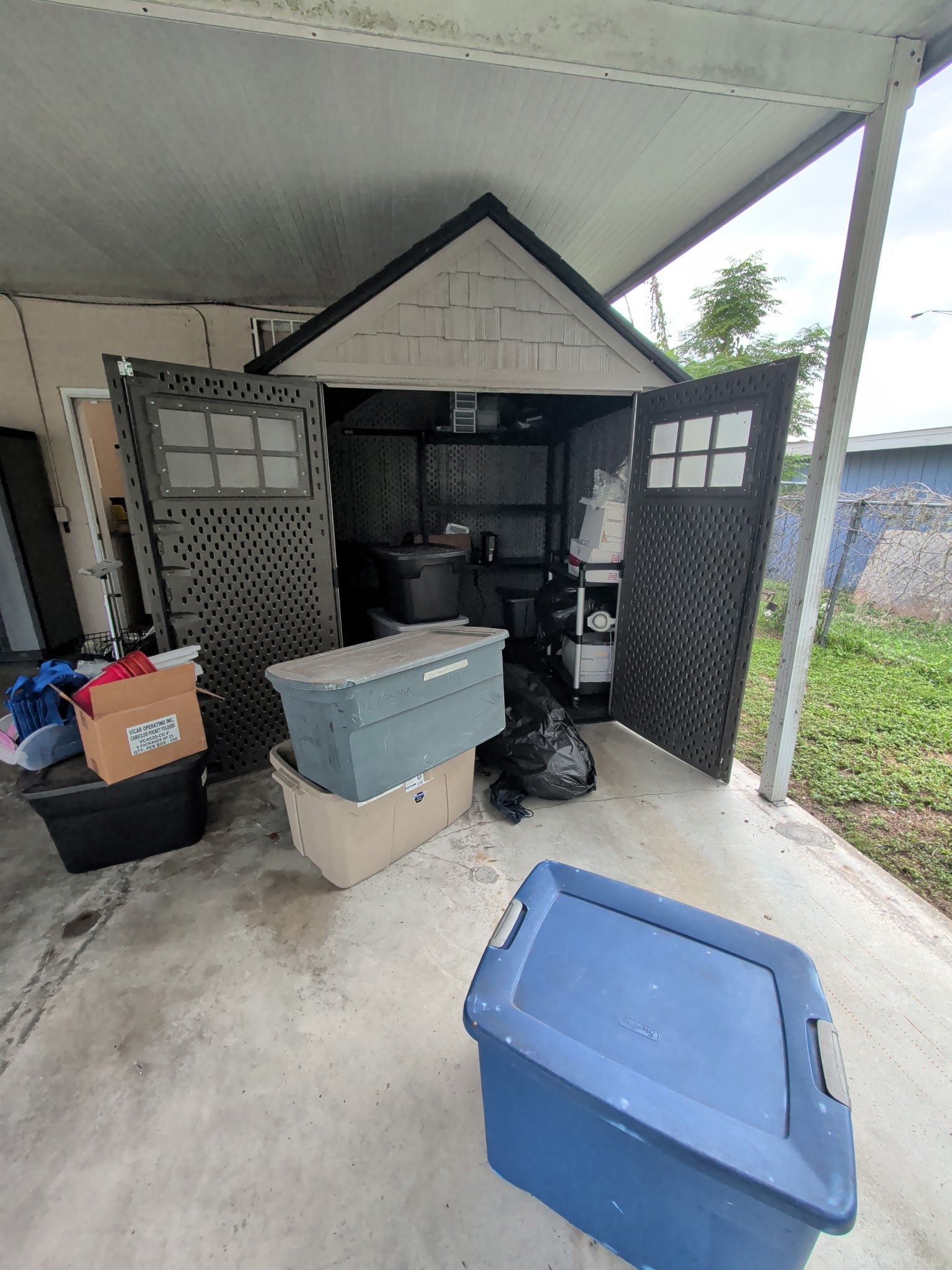 The shed at its original location on a concrete floor beneath a metal covering