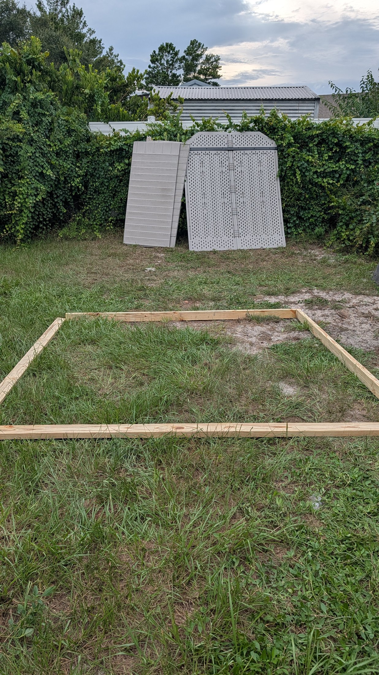 Disassembled shed panels and a wooden base frame laid out on grass