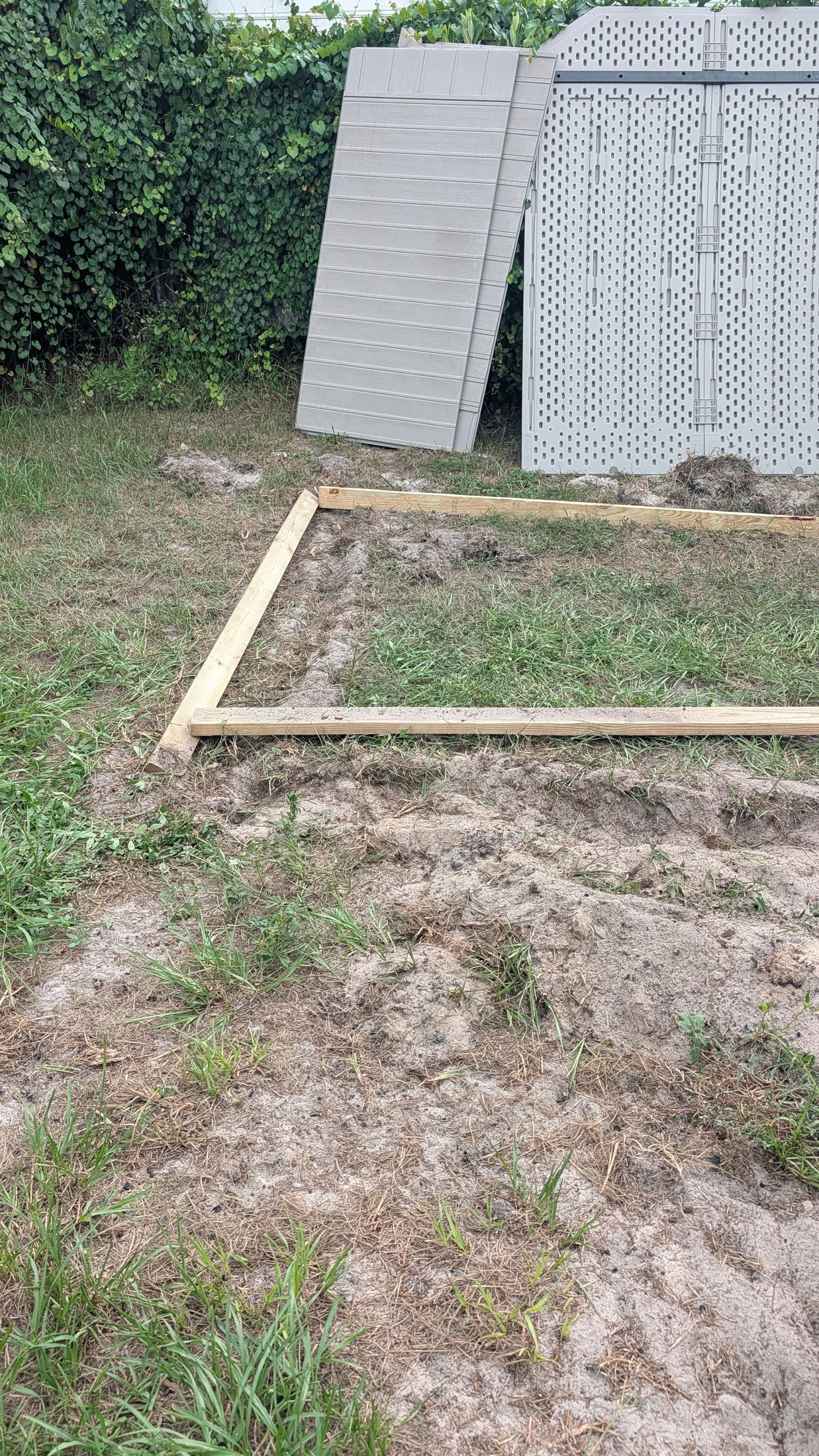 Wooden leveling frame resting on uneven sandy ground beside shed panels